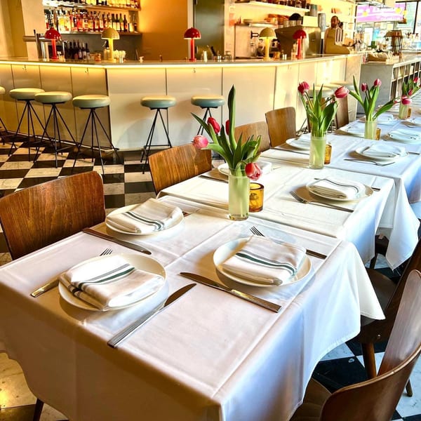 Set tables with white tablecloths and tulip centerpieces, with a bar and stools in the background.