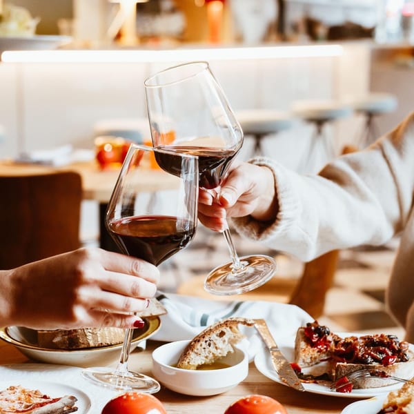 Two people clinking glasses of red wine at Pecoraro Latteria, with Italian food on the table.