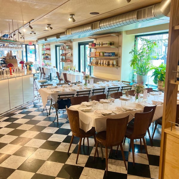 Pecoraro Latteria's dining room with checkered floors, set tables, a bar, and shelves of Italian products.