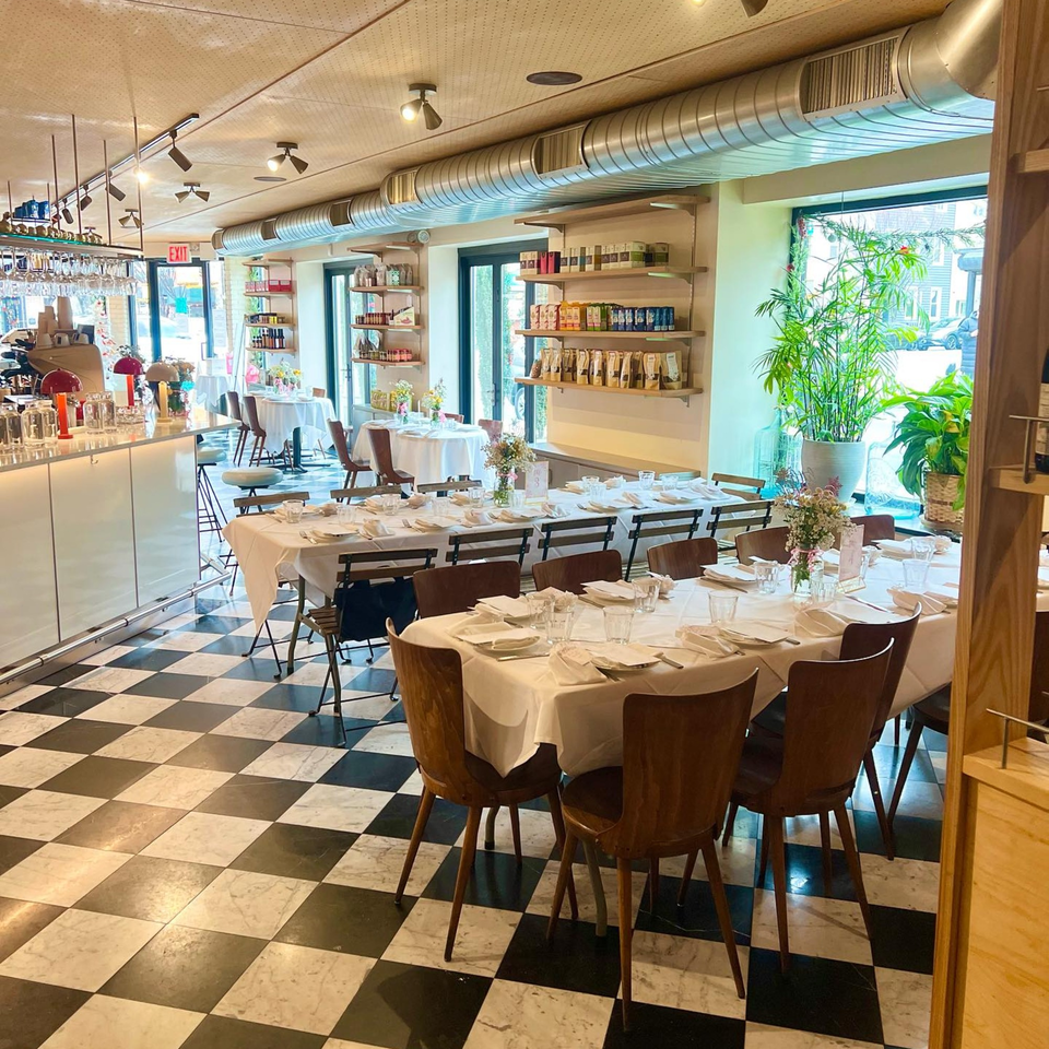 Pecoraro Latteria's dining room with checkered floors, set tables, a bar, and shelves of Italian products.