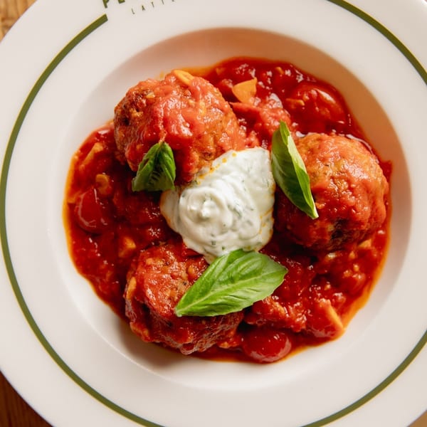 Italian meatballs in rich tomato sauce with a dollop of white cream and fresh basil leaves.