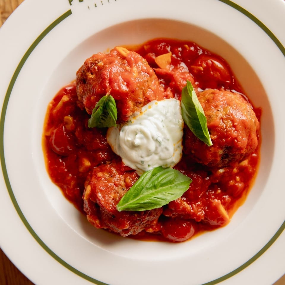 Italian meatballs in rich tomato sauce with a dollop of white cream and fresh basil leaves.