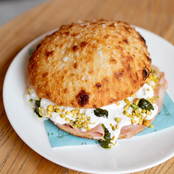 Pecoraro Latteria's focaccia sandwich with prosciutto, burrata, pesto, and pistachios on a white plate.