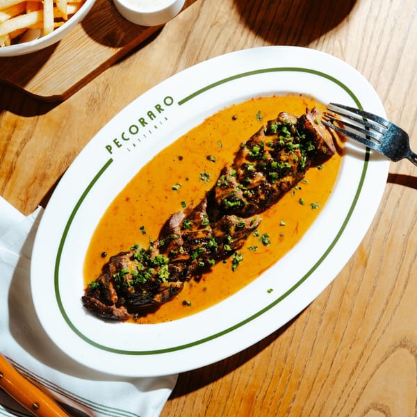 Grilled meat in a rich orange sauce, garnished with chives, on a white Pecoraro Latteria plate.