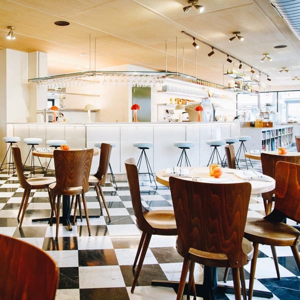 Interior of Pecoraro Latteria, an Italian restaurant, with checkered floors, wooden tables, and a white bar.