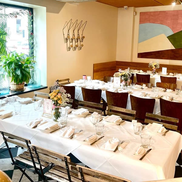 A dining room at Pecoraro Latteria with long tables set for a banquet, featuring white tablecloths and floral centerpieces.