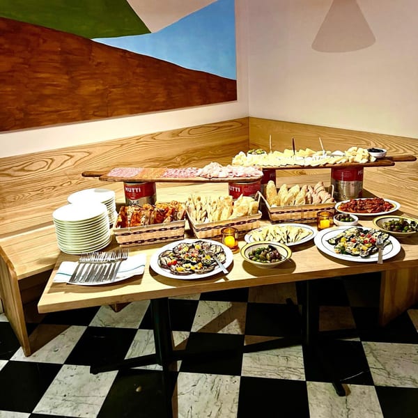 A Pecoraro Latteria buffet table laden with Italian appetizers, cheeses, meats, and bread on a checkered floor.