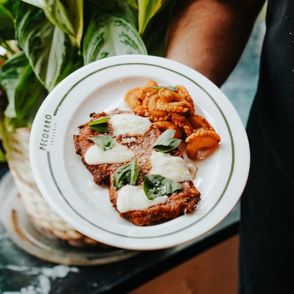 Pecoraro Latteria's chicken parmesan with fresh basil and pasta, held by a server.