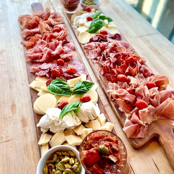 Two long wooden boards filled with Italian meats, cheeses, cherry tomatoes, and basil.