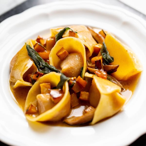 Close-up of Italian pasta dish with large pasta shells, diced vegetables, and sage in a rich sauce.