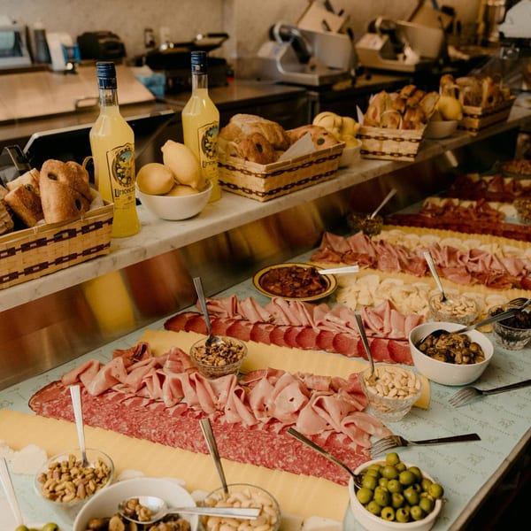 A long Italian charcuterie spread with meats, cheeses, olives, nuts, bread, and Limoncello bottles.