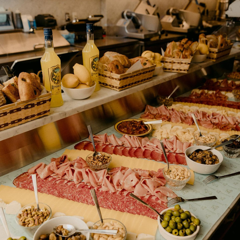 A long Italian charcuterie spread with meats, cheeses, olives, nuts, bread, and Limoncello bottles.