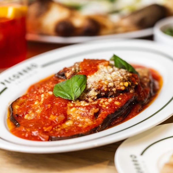 Eggplant parmesan with rich tomato sauce, grated cheese, and fresh basil on a white plate.